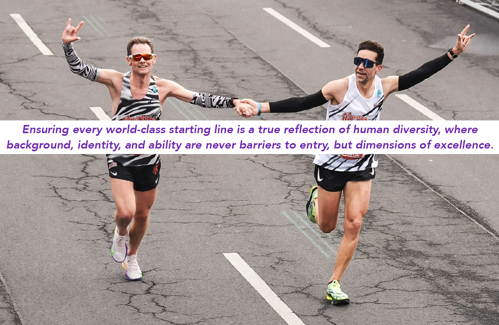 Deaf runners Thomas Eller (left) and Matteo Anson Valeri (right) holding hands and throwing hand signs while running down an asphalt road during a race.