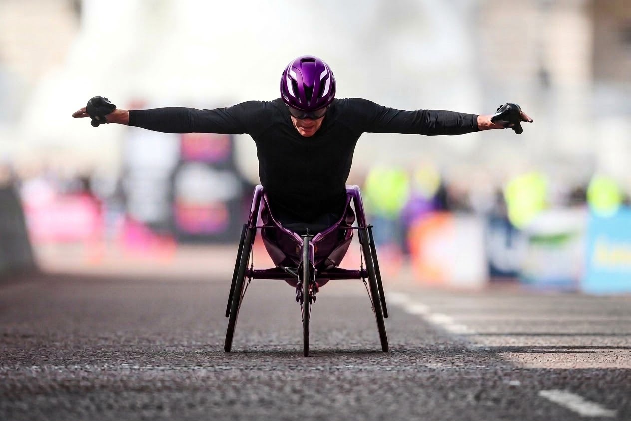 Wheelchair racer wearing a purple helmet racing on a city road with arms outstretched.